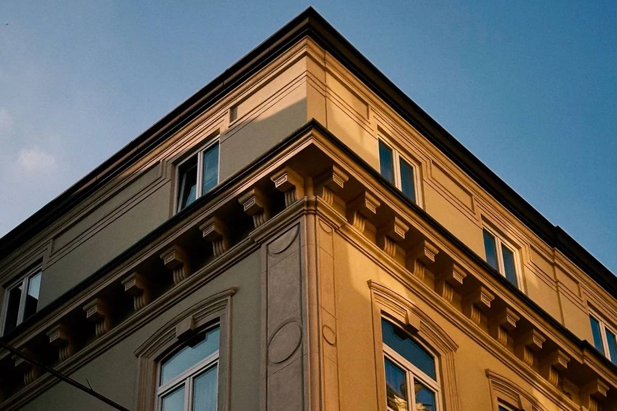 Altbausanierung: Detailaufnahme einer historischen Gebäudeecke im Abendlicht mit professionell gestrichener Fassade und sauber erhaltenen Stuckelementen.