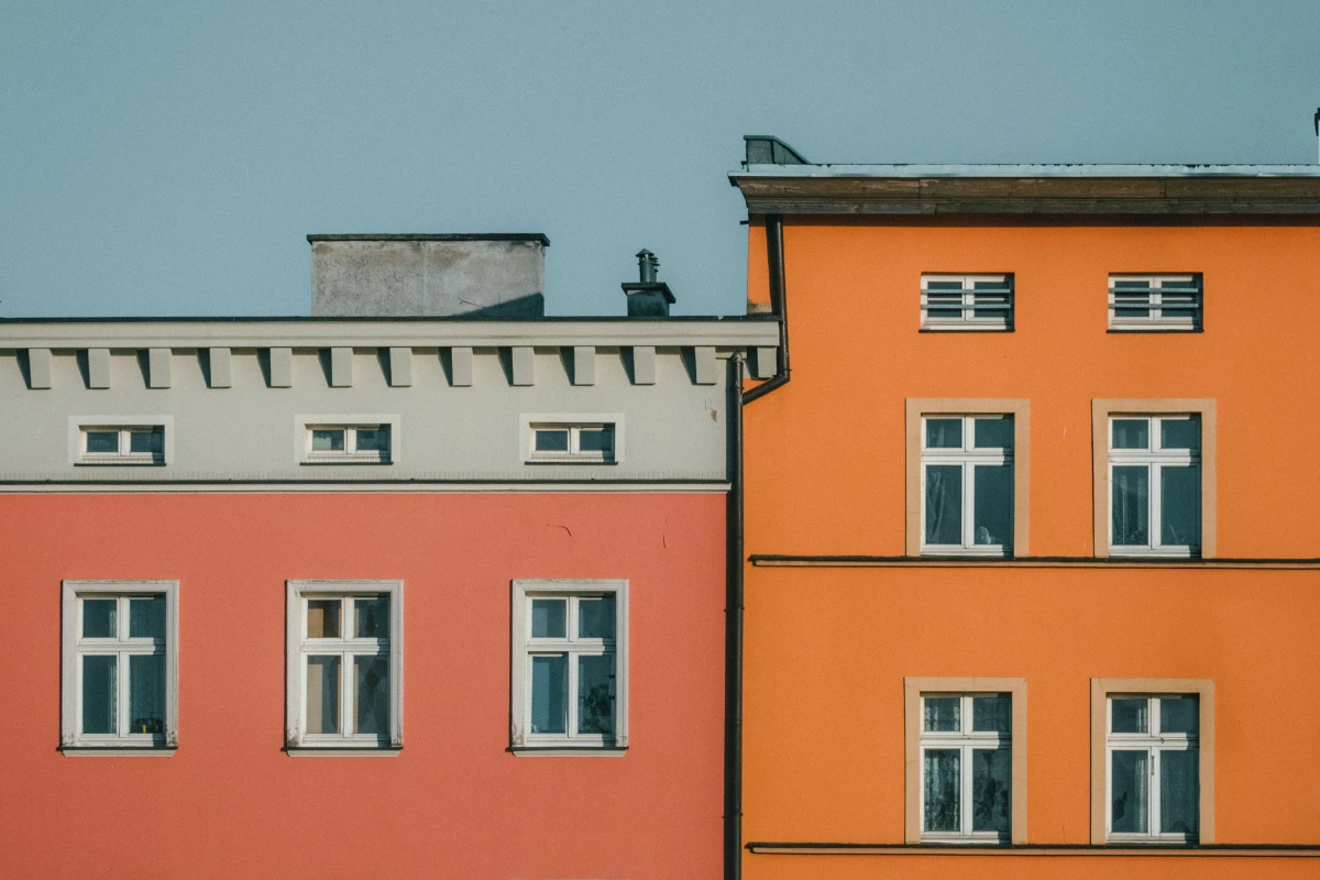 Fassadengestaltung: Zwei aneinandergrenzende, frisch gestrichene Hausfassaden in harmonisch kontrastierenden Terrakotta- und warmen Orangetönen.