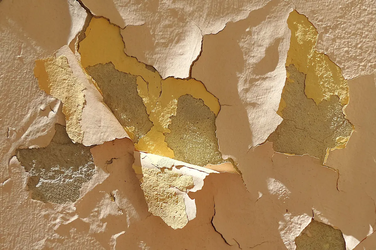 Renovationsputz und Untergrundvorbereitung: Nahaufnahme einer reparaturbedürftigen Wandmauer mit stark abblätternder, alter Farbe und oberster Putzschicht.