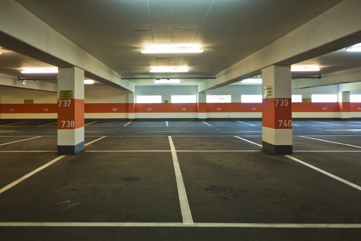 Bodenmarkierungen und Leitsysteme: Sauber gezogene weiße Parkplatzlinien und farbig markierte Säulen zur Orientierung in einer Tiefgarage.